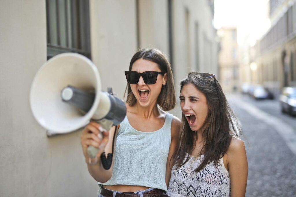 Cheerful young women screaming into a loudspeaker