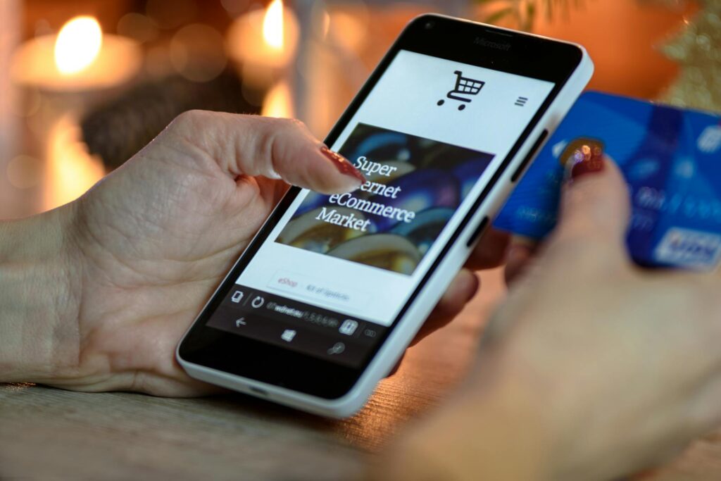 a person using a black and white smartphone and holding a blue card-benefits of e-commerce for small businesses
