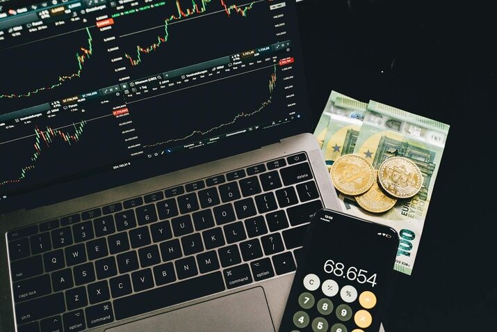 A display of bitcoins and paper money beside a mobile phone and laptop with graphs on the screen-fintech websites
