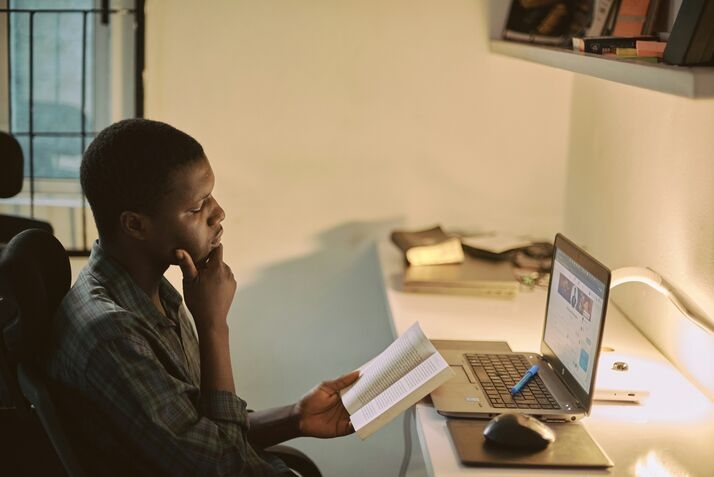  man in a gray dress shirt holding a book in front of a laptop-edge computing
