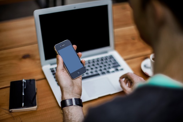  Person holding a black iPhone in front of a laptop