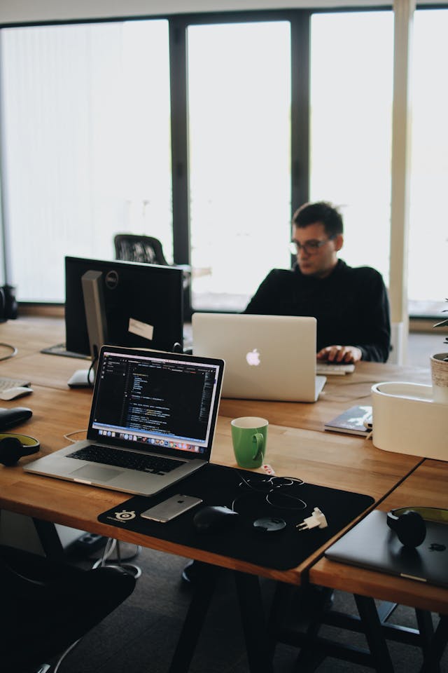 A man in a black shirt sits behind a desk with computers