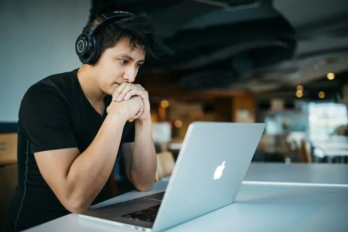 man wearing headphones while sitting on chair in front-of macbook