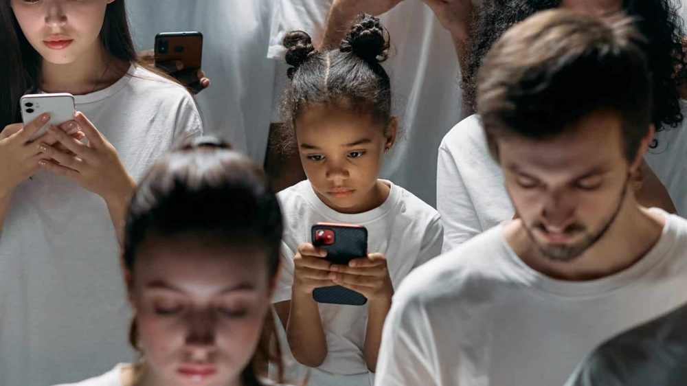 A diverse group standing around each other using cell phones.
